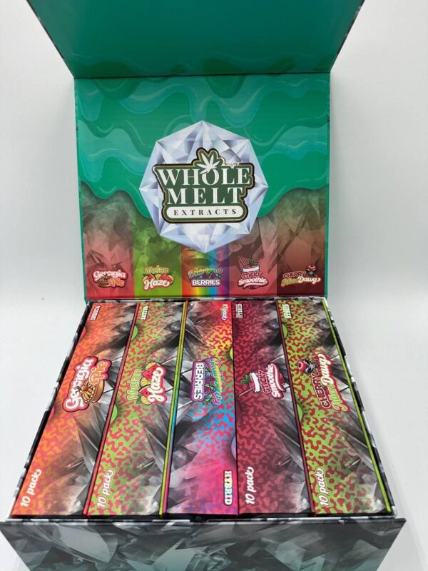 An open display box shows five rows of colorful, branded candy packaging from "Whole Melt Melon Haze." The interior lid showcases the green and white Whole Melt Melon Haze logo with a bright, patterned background. Each package in the box is vividly designed and labeled.