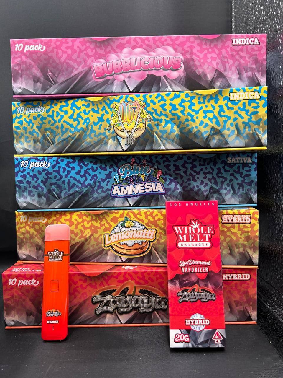 A stack of colorful Import placeholder for 49 boxes towers on a table. The boxes are labeled with various strains: Dubblicious, Zaza, Blue Amnesia, Lemonatti Hybrid, and more. In front, there are two vape pens and additional packaging for Whole Melt Extracts.