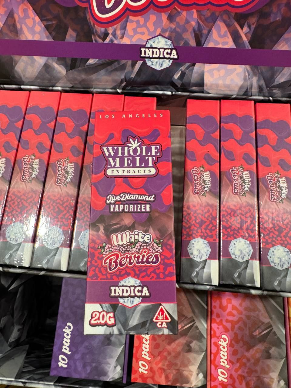 A display of **Import placeholder for 63** is shown. The packaging is predominantly purple and red with a berry motif. Each box is labeled as indica, 2.0g, and includes the Cannabis CA symbol. The boxes are organized in a retail setup.