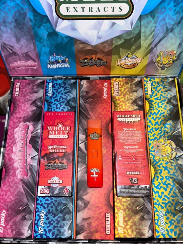 An assortment of colorful "Whole Melts Zayaya" vape product boxes is displayed, showcasing various flavors and types of extracts. In the center, a red vape pen is positioned vertically. The background boxes have diverse patterns and labels indicating different cannabis extracts.
