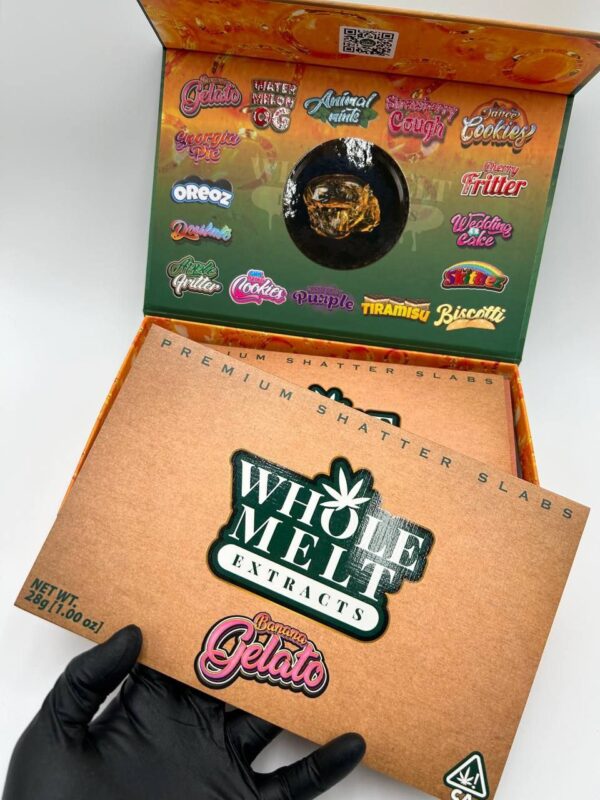 A hand in a black glove holds a box labeled "Whole Melt Extracts, Premium Shatter Slabs." The open box reveals a collection of cannabis shatter with various strain names such as "Whole Melt Banana Gelato," "Wedding Cake," and "Animal Mintz.