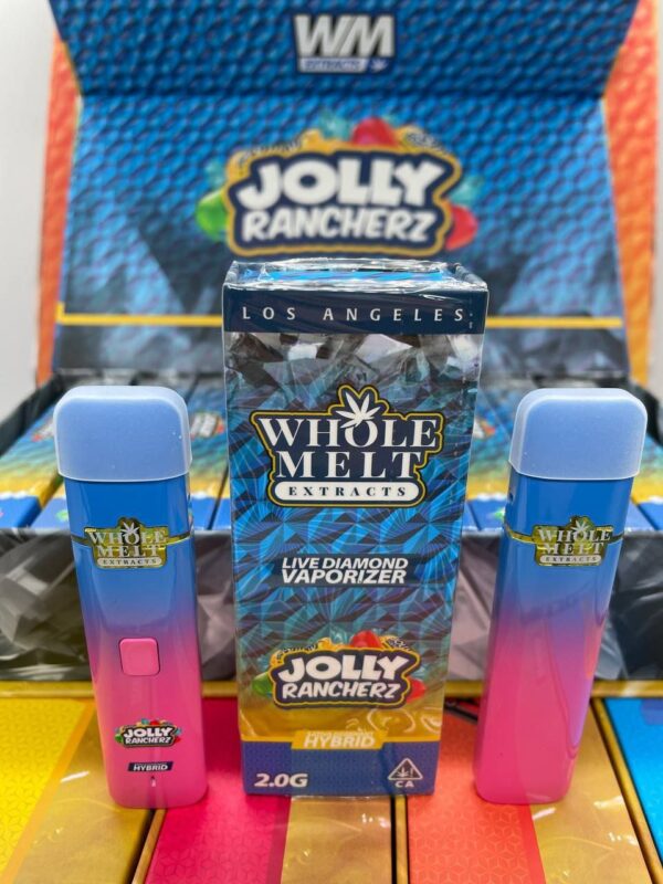 Image of two Whole Melt Jolly Rancherz flavored live diamond vaporizers from Whole Melt Extracts positioned on either side of a box with the same branding. The vaporizers are blue and pink, and the packaging features colorful Jolly Rancher graphics and text.