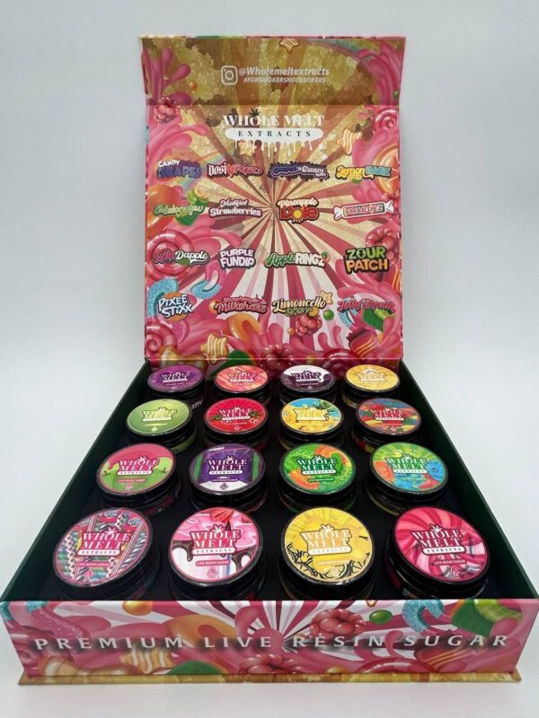 An open colorful box displaying 18 circular containers of cannabis extracts with unique, vibrant labels. The box lid showcases various strain names and graphics, highlighted by a candy-themed design. Text at the bottom reads "Whole Melts Candy Edition.