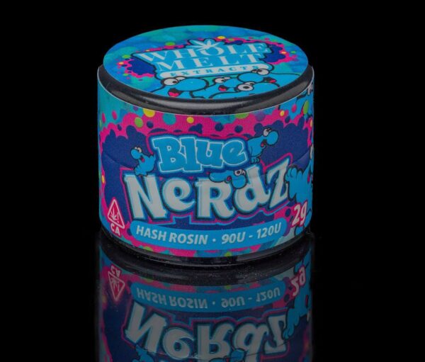 A small, round container with a colorful, vibrant design featuring splashes of blue, pink, and yellow. The label reads "Blue Nerdz Hash Rosin" and "90U - 120U" along with a "Whole Melt Extracts" logo at the top. The container's reflection is visible on the black surface.